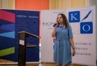Kobieta stoi na scenie, w ręce trzyma mikrofon.