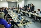 Sala konferencyjna, ludzie siedzą przy stołach.
