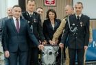 Jadwiga Wójtowicz trzyma ze strażakami strażacki sprzęt.