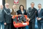 Jadwiga Wójtowicz trzyma ze strażakami strażacką pompę.
