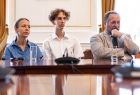 Uczeń w dłuższych kręconych włosach siedzący wśród nauczycieli.