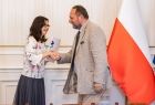 Mężczyzna w jasnym garniturze w uścisku dłoni z kobietą.