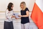 Kobieta w czarnej bluzce odbierająca list gratulacyjny.