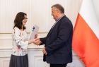 Starszy mężczyzna w ciemnym garniturze odbierający gratulacje.