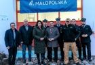 Uczestnicy wydarzenia stoją przed brama remizy. Nad nimi widoczny napis Małopolska.