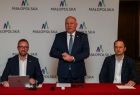 Wicemarszałek Ryszard Pagacz stoi przy stole. Obok siedzi dwóch mężczyzn.