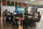 młodzież siedzi przy stole przed komputerami i pracuje nad zadaniem Hackathonowym