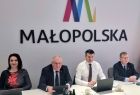 Zarząd Województwa Małopolskiego siedzi przy stole. Za nim widoczny napis Małopolska.