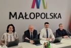 Czteroosobowy Zarząd Województwa Małopolskiego siedzi przy stole. Za nimi na ścianie napis Małopolska.