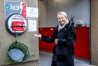 Iwona Gibas z zarządu województwa stojąca obok nowoczesnego defibrylatora zamontowanego przy drzwiach strażackiej remizy