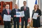 Wicemarszałek Witold Kozłowski i trzy osoby z teczkami w dłoniach.