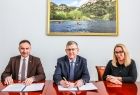 Wicemarszałek Witold Kozłowski w trakcie podpisywania umowy. Obok kobieta i mężczyzna.