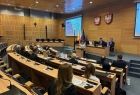Kobieta przemawiająca z mównicy do słuchaczy. W tle projektor z wyświetlanymi slajdami.