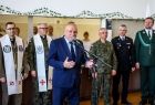 Wicemarszałek Ryszard Pagacz stoi przy mikrofonie. Za nim widoczni księża i żołnierze.