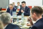 Marszałek Łukasz Smółka siedzi przy stole i trzyma mikrofon w ręce.