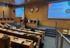 Kobieta przemawiająca z mównicy do słuchaczy. W tle projektor z wyświetlanymi slajdami.
