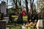 Żołnierze idą przez cmentarz ze sztandarem.