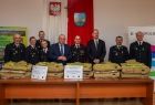 Uczestnicy wydarzenia stoją na sali. Na stołach przed nimi leżą mundury.