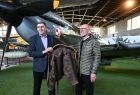 Richard Dajda przekazuje na ręce Tomasza Koseckiego kurtkę lotniczą swojego ojca. Panowie stoją na tle samolotu Spitfire w Hangarze głównym Muzeum Lotnictwa Polskiego w Krakowie.