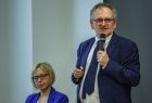 Mężczyzna w garniturze stoi i trzyma w ręce mikrofon.