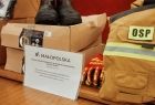 Strażacki ekwipunek, w tym bojowy uniform w pustynnym kolorze, para wysokich butów oraz kartka z napisem Małopolska 