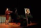Młoda artystka grająca na skrzypcach, obok stojący portret śp. ks. Tadeusza Isakowicza-Zaleskiego 
