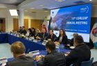 Grupa osób przy stole prezydialnym. W tle duży ekran.