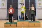 Trzech chłopców stojących na podium z numerami 1,2,3. Chłopcy trzymają dyplomy i puchary