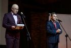 Wojciech Skruch stoi na scenie. Obok stoi przy mikrofonie mężczyzna.