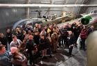 zwiedzający słuchają wykładu mistrza Jana Hofmanna w Hangarze Łukowym, w tle widać śmigłowiec