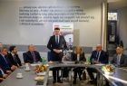Marszałek Łukasz Smółka stojący wśród ludzi siedzących wokół stołu. 