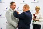 Wojewoda przypina odznaczenie panu Tomaszowi Wichmanowi. Obok z różą w ręku stoi Iwona Gibas z zarządu województwa