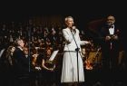 Iwona Gibas z Zarządu Województwa Małopolskiego przemawiająca na scenie. W tle członkowie orkiestry symfonicznej