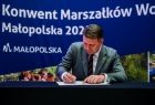 Mężczyzna w zielonym garniturze podpisuje dokument.