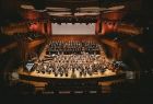 Zdjęcie przedstawia zespół muzyczny Filharmonii Krakowskiej im. Karola Szymanowskiego, stojący na scenie.