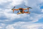 Pomarańczowy dron z kamerą w czasie lotu.
