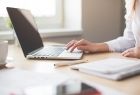 kobieta pisząca na laptopie, obok leży papierowy zeszyt