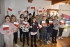 Grupa dzieci z biało-czerwonymi chorągiewkami i stojący za nimi baner reklamowy Małopolski