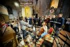 Muzycy grający na instrumentach smyczkowych oraz członkowie kilkuosobowego chóru podczas występu w zabytkowym kościele
