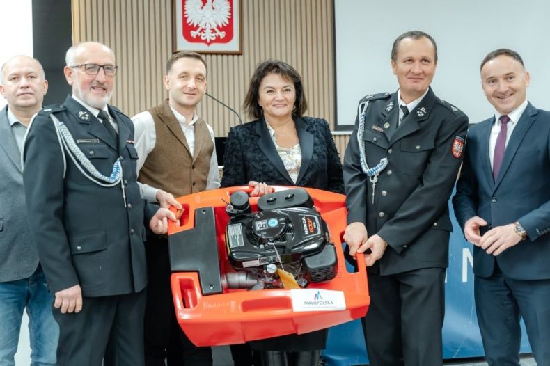Jadwiga Wójtowicz trzyma ze strażakami strażacką pompę.