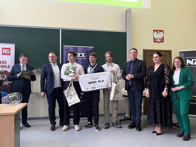 Studenci stojący na środku sali wykładowej, odbierający nagrody i wyróżnienia