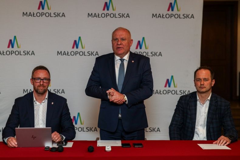 Wicemarszałek Ryszard Pagacz stoi przy stole. Obok siedzi dwóch mężczyzn.