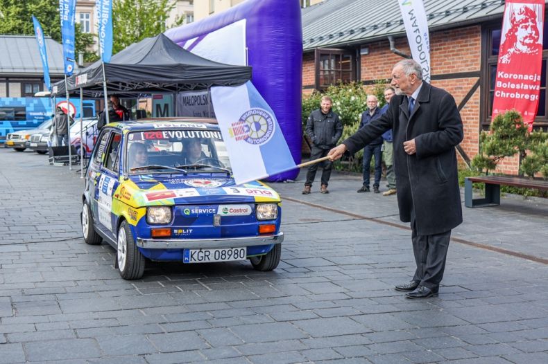 Profesor Jan Tadeusz Duda macha flagą przed samochodem na starcie.