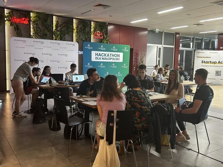 młodzież siedzi przy stole przed komputerami i pracuje nad zadaniem Hackathonowym