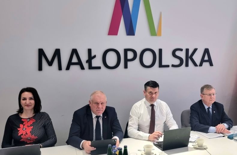 Zarząd Województwa Małopolskiego siedzi przy stole. Za nim widoczny napis Małopolska.