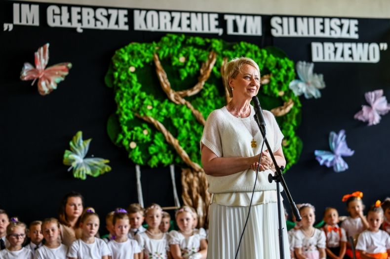 Iwona Gibas z zarządu województwa zwraca się do uczestników wydarzenia. Za panią marszałek siedzą dzieci, które przygotowały program artystyczny. W tle, na ścianie, znajduje się makieta drzewa, a nad nim napis: Im głębsze korzenie tym mocniejsze drzewo
