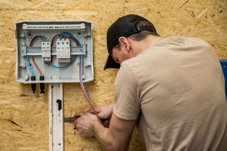 Uczeń montuje skrzynkę elektryczną na ścianie.