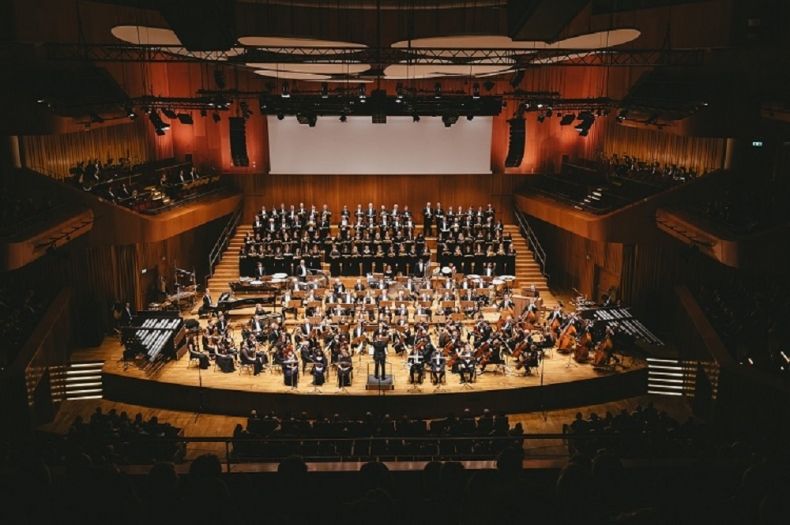 Zdjęcie przedstawia zespół muzyczny Filharmonii Krakowskiej im. Karola Szymanowskiego, stojący na scenie.