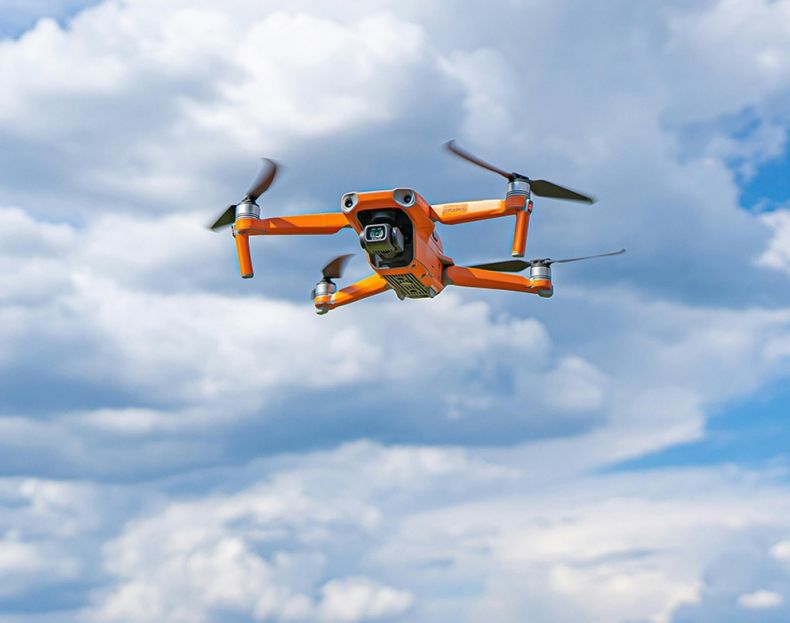 Pomarańczowy dron z kamerą w czasie lotu.