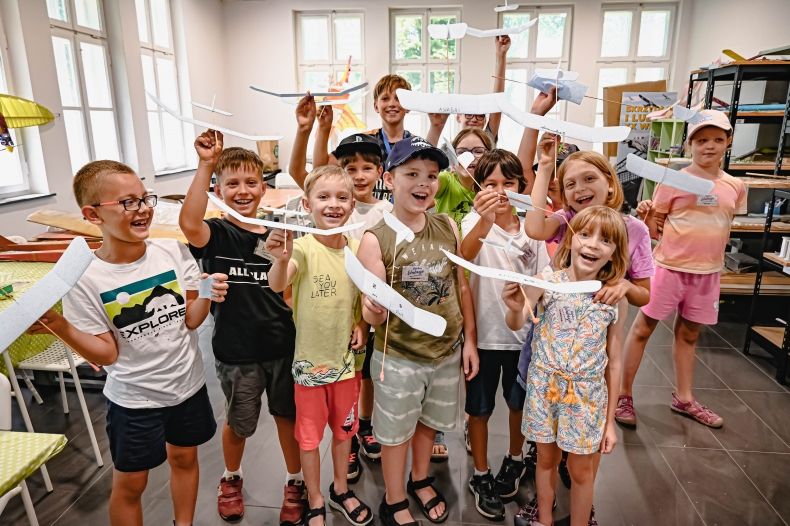 grupa roześmianych dzieci trzyma w rękach modele samolotów z balsy